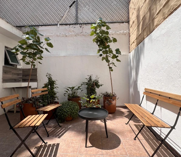 Imagen de un patio con una banca y dos sillas junto a una mesa